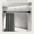 Matte black tension rod pressed between two tiled bathroom walls with a grey shower curtain
