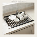 Roll-up stainless drying rack unrolled across a kitchen sink with plates, bowls and mugs on it