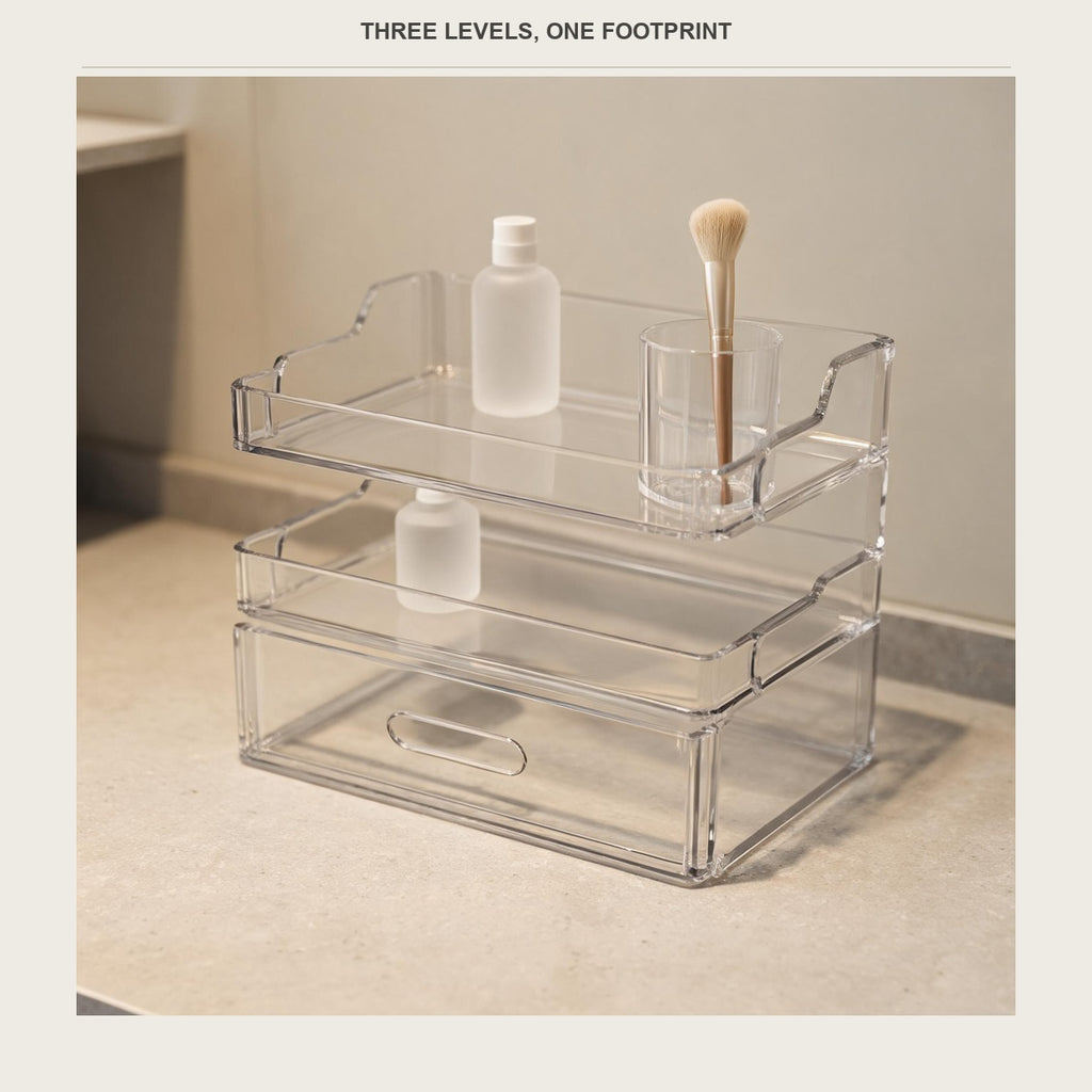 Clear acrylic 3-tier vanity organizer on a pale bathroom counter holding unbranded white bottles