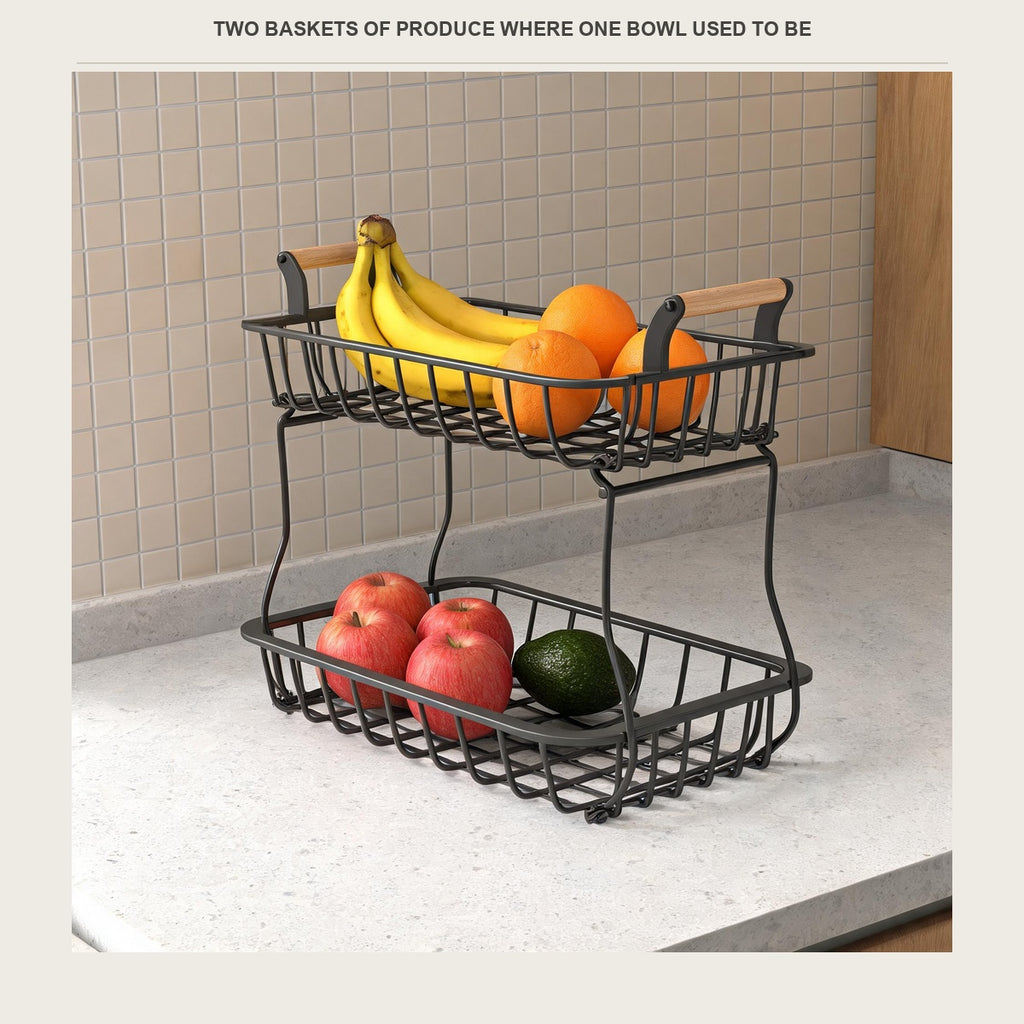 Two-tier wire fruit basket on a kitchen counter holding bananas, oranges and apples