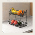 Two-tier wire fruit basket on a kitchen counter holding bananas, oranges and apples