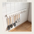 White kitchen utensil rail on a tiled splashback holding wooden handled cooking tools