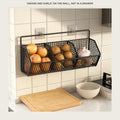 Black wire wall basket with onions, potatoes and garlic in its three compartments above a kitchen counter