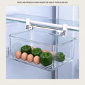 Clear pull-out drawer hanging under a fridge shelf on a white rail with eggs and peppers inside