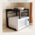 Microwave sitting under a black steel counter rack with jars on the shelf above