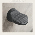 Black suction shower foot rest mounted on a tiled shower wall