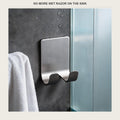 Stainless steel razor holder stuck on a bathroom wall with a razor hanging from it