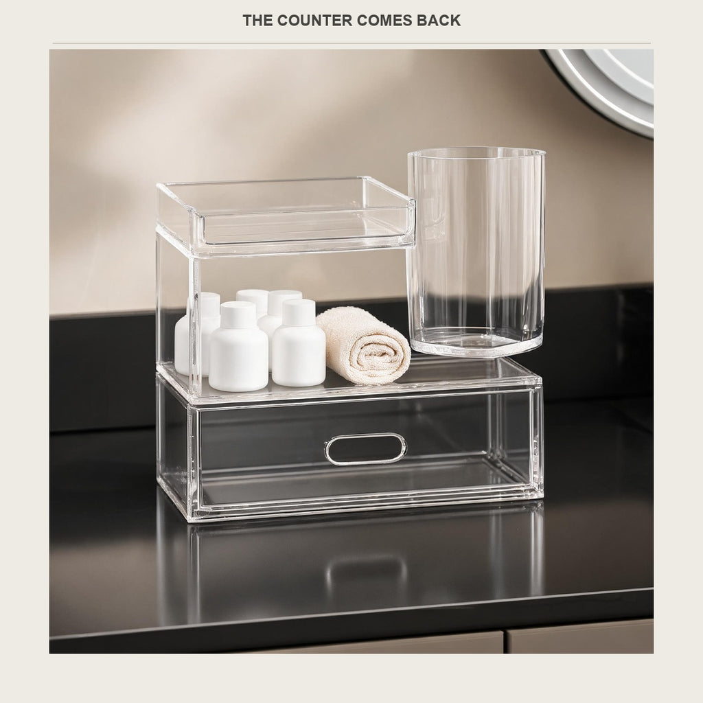 The acrylic vanity organizer on a wide empty bathroom counter with only a folded towel beside it