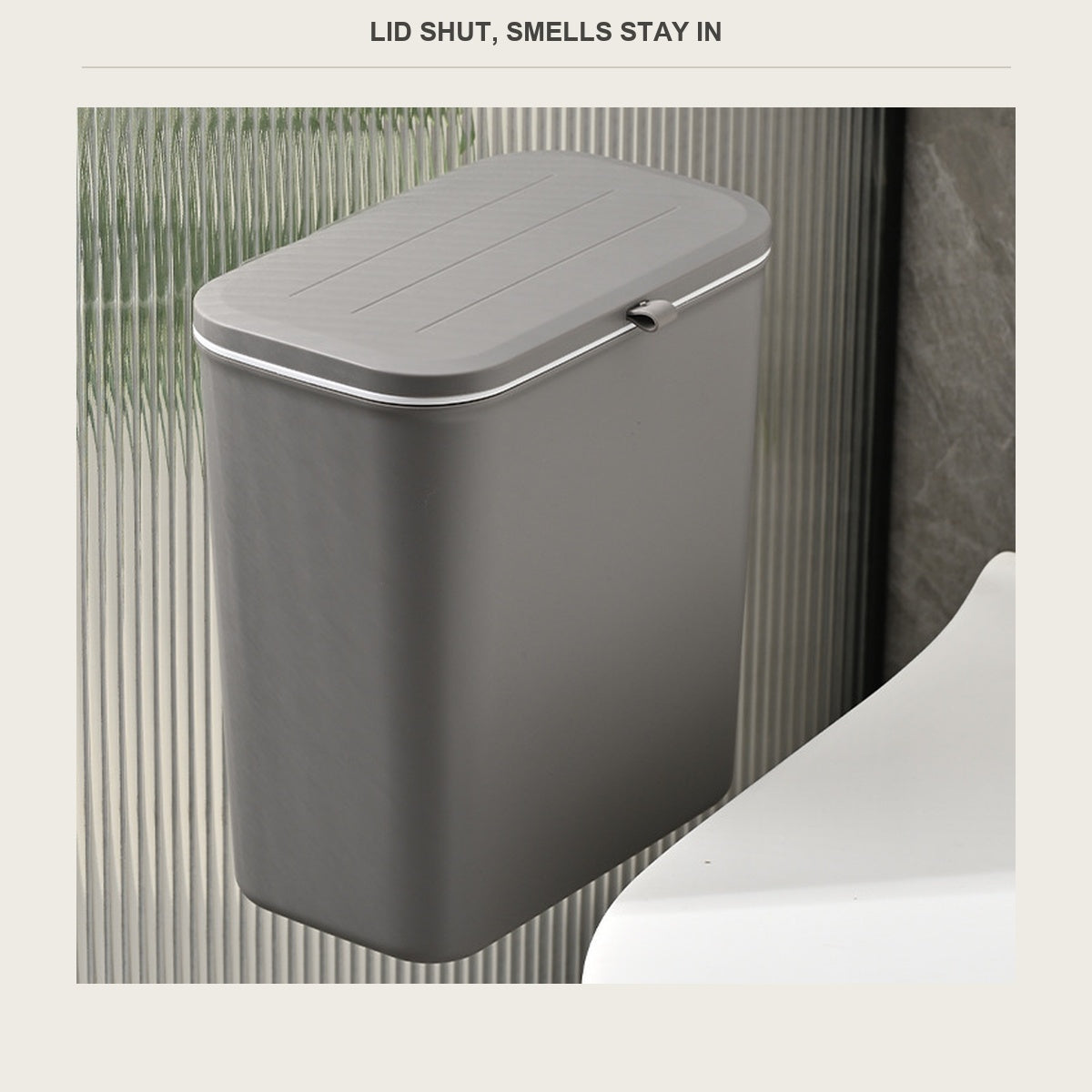 Grey hanging trash bin with the lid shut, mounted on a bathroom wall