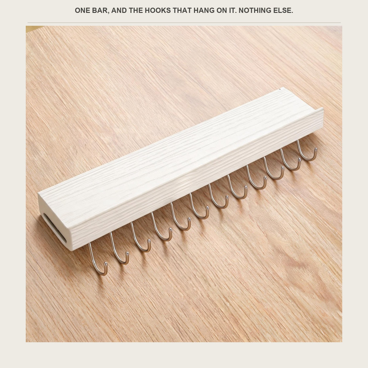 The utensil rail laid on a pale wood counter with its hooks beside it