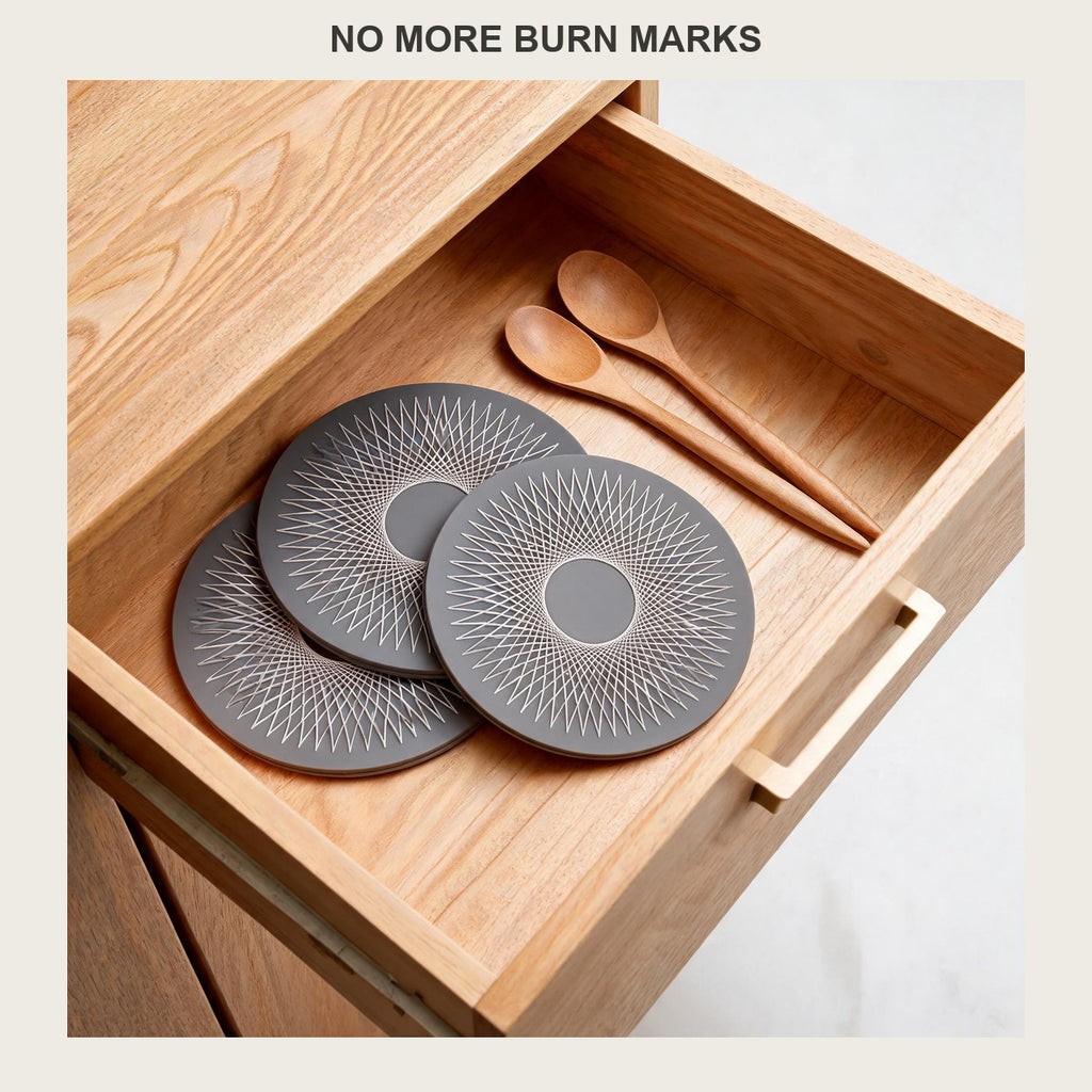 Three round silicone trivet mats stacked flat in an open kitchen drawer with wooden spoons