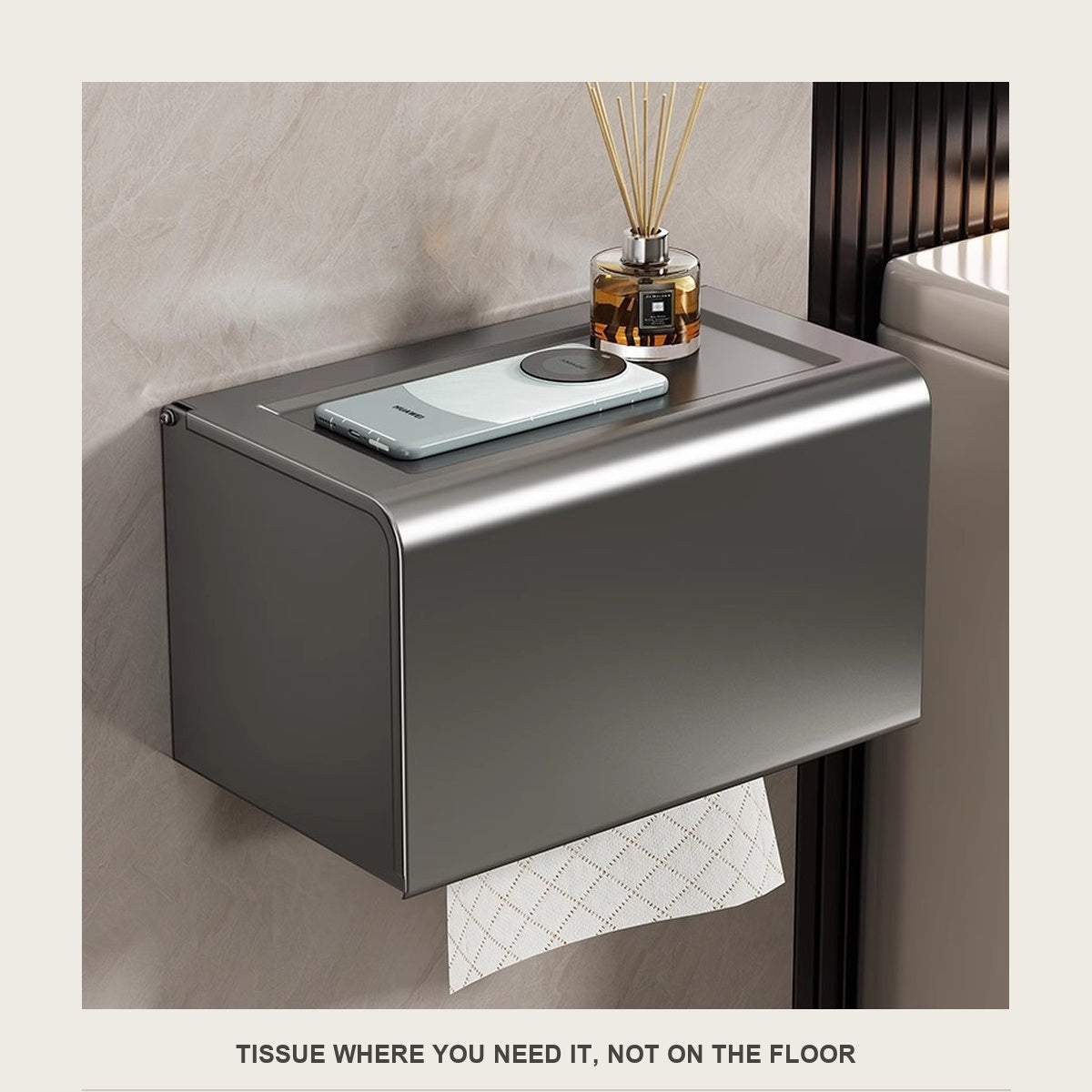 Wall mounted tissue box on a tiled bathroom wall with a phone and diffuser on top