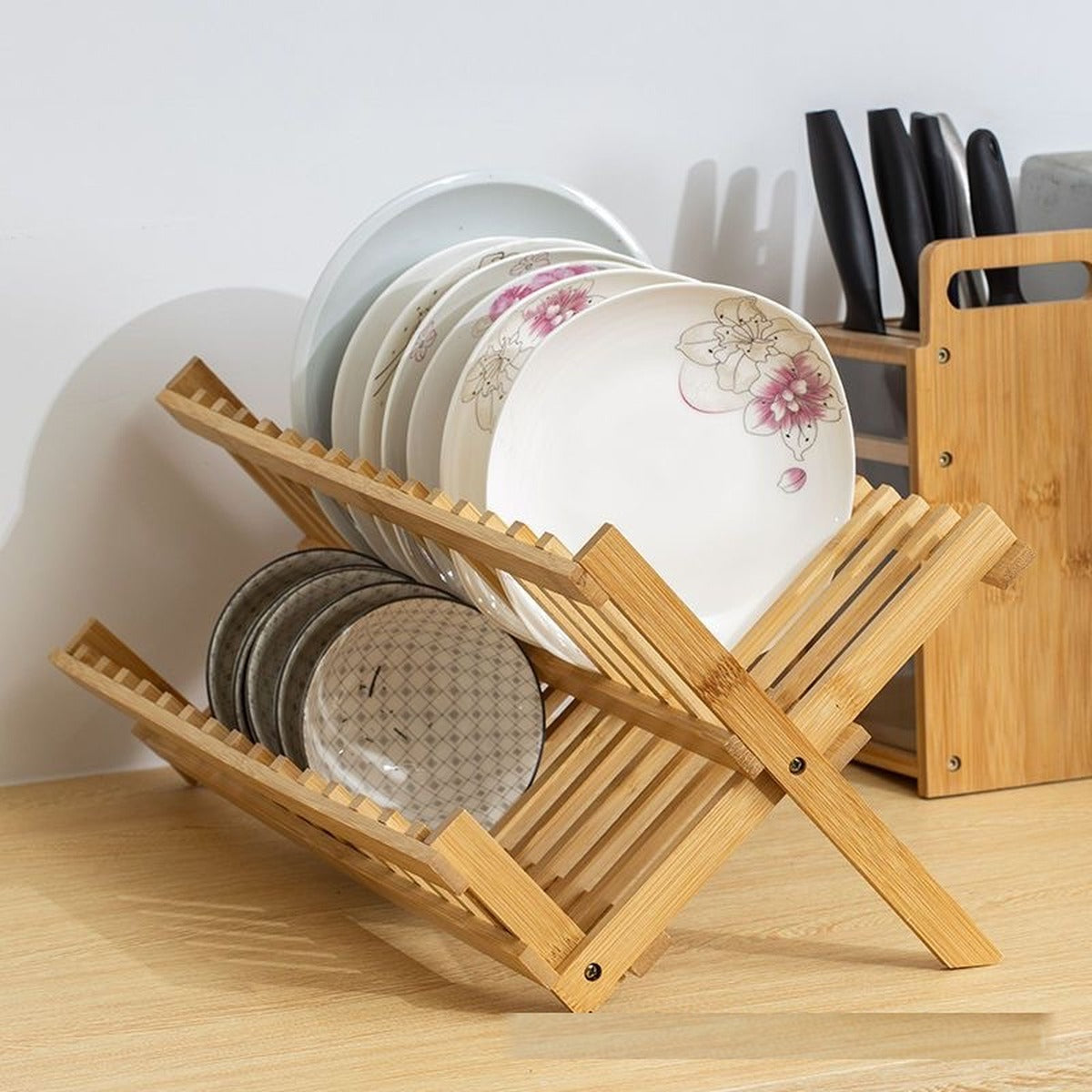 Folding bamboo dish rack holding dinner plates on top and side plates below, beside a knife block