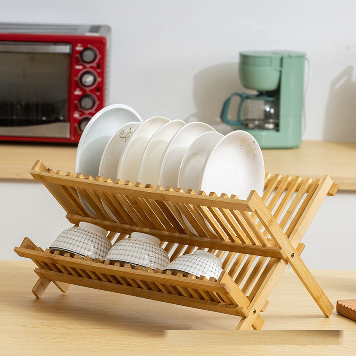 Two-tier bamboo dish rack on a kitchen counter with a red toaster oven and a stand mixer behind it